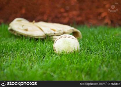Closeup horizontal photo of old baseball with glove in background on natural grass field