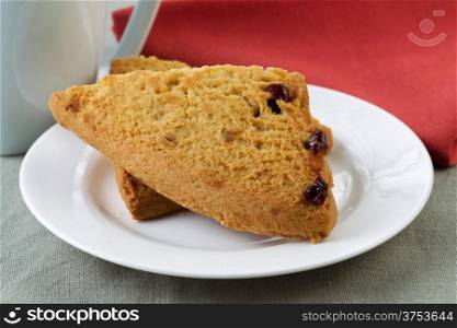 Closeup horizontal photo of scones on white plate with tea cup plus red napkin in background