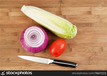Closeup horizontal top view photo of fresh whole red onion, lettuce and tomato with kitchen knife beside and natural bamboo wood underneath