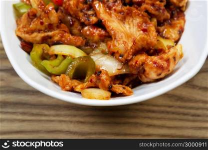 Closeup horizontal view of Chinese spicy chicken dish in white bowl with rustic wooden boards underneath