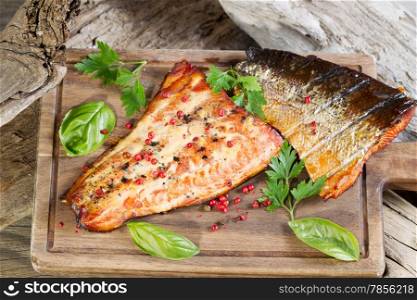 Closeup horizontal view of smoked salmon fillets with seasoning inside of drift wood on serving board