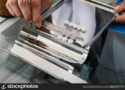 Closeup image hand of pharmacist counting and arrange pills on qualified stainless counting tray with spatula in pharmacy. Pharmacist prepare medication in stainless tray by prescription at drugstore.