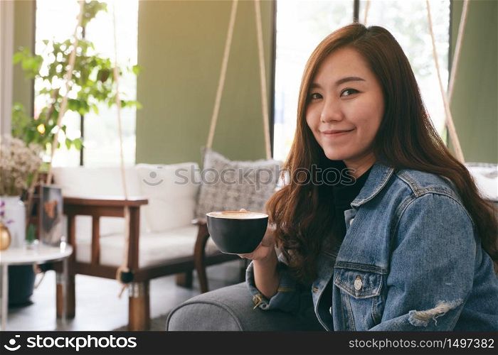 Closeup image of a beautiful asian woman holding and drinking hot coffee in cafe