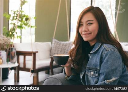 Closeup image of a beautiful asian woman holding and drinking hot coffee in cafe