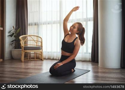 Closeup image of a beautiful young asian woman sitting on training mat and stretching her arms to warm up before workout at home
