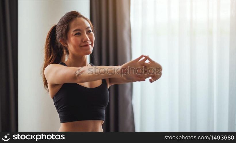 Closeup image of a beautiful young asian woman stretching her arms to warm up before workout at home