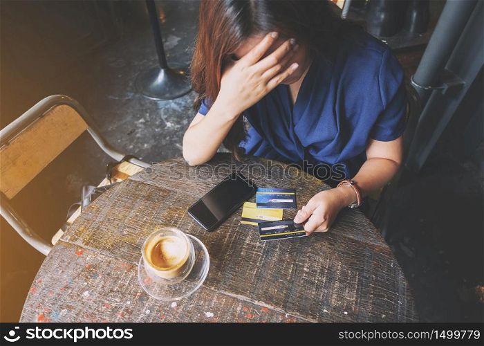 Closeup image of an Asian woman get stressed and broke while holding credit card with mobile phone on the table