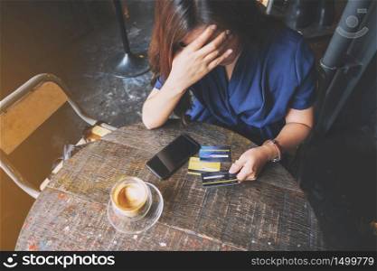 Closeup image of an Asian woman get stressed and broke while holding credit card with mobile phone on the table
