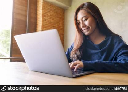 Closeup image of an asian woman working and typing on laptop computer on wooden table
