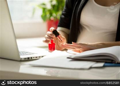 Closeup image of businesswoman painting fingernails at work