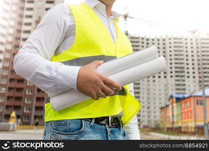 Closeup image of engineer in safety vest holding rolled blueprints