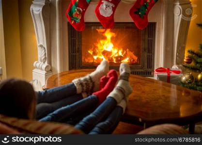 Closeup image of family in cosy knitted socks warming at fireplace decorated for Christmas