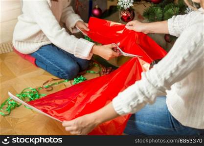 Closeup image of girl cutting red wrapping paper for Christmas presents