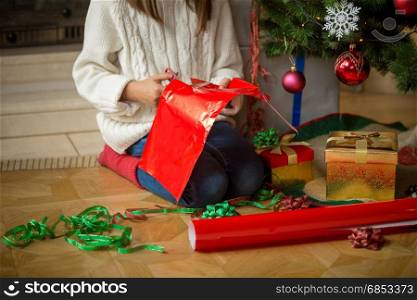 Closeup image of girl wrapping presents under Christmas tree