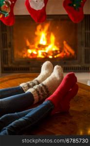 Closeup image of male and female feet in woolen socks warming at burning fireplace