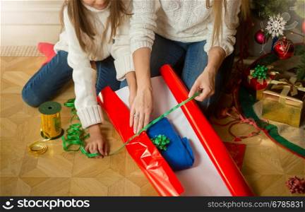 Closeup image of mother and daughter making Christmas present and wrapping woolen sweater in red wrapping paper
