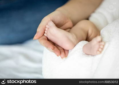 Closeup image of mother holding newborn baby feet on bed