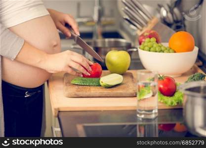 Closeup image of pregnant woman cutting vegetables on wooden board