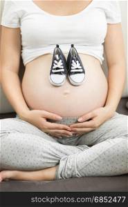 Closeup image of pregnant woman holding baby boy shoes on belly