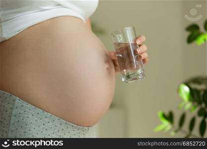 Closeup image of pregnant woman holding glass of water