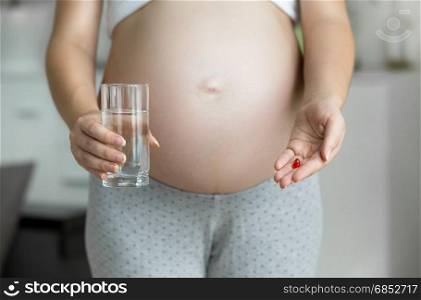 Closeup image of pregnant woman holding pill in hand