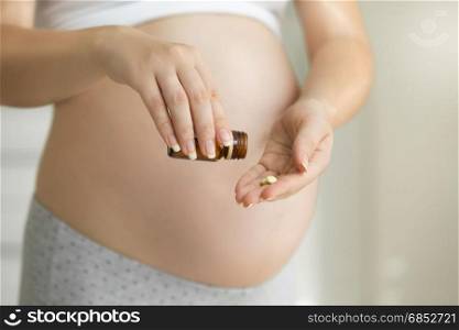 Closeup image of pregnant woman holding pills and medicine bottle