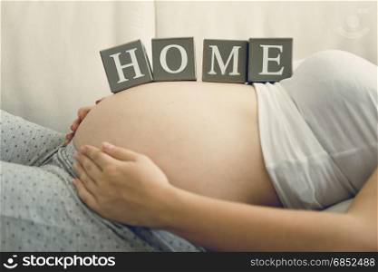 Closeup image of pregnant woman holding word Home on belly