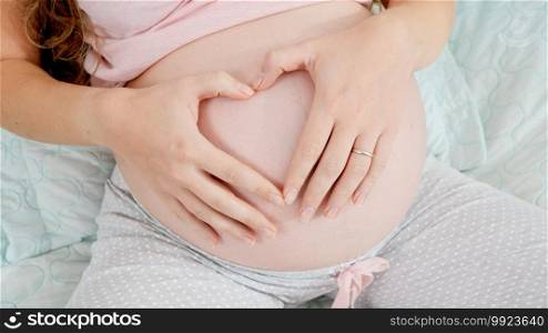 Closeup image of pregnant woman stroking belly and making shape of heart. Concept of expecting child, love and parenting. Closeup image of pregnant woman stroking belly and making shape of heart. Concept of expecting child, love and parenting.