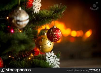 Closeup image of red and golden baubles hanging on Christmas tree on background of burning fireplace