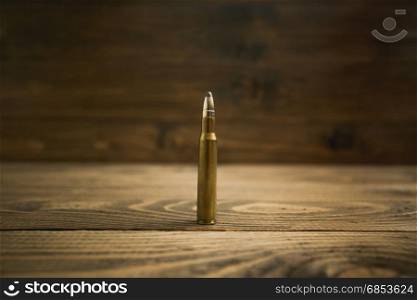 Closeup image of riffle bullet on old wooden desk