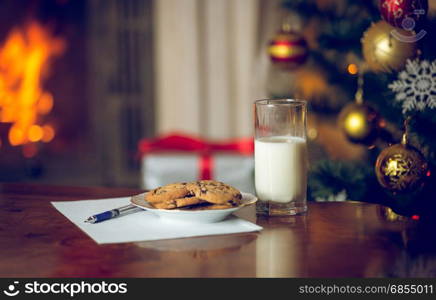 Closeup image of treats and letter to Santa on wooden table next Christmas tree