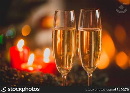 Closeup image of two glasses of Champagne in front of burning candles and lights.