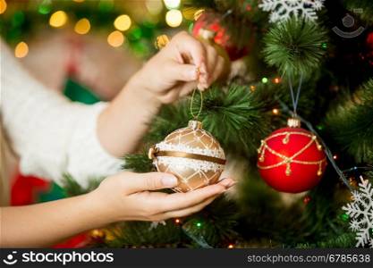 Closeup image of woman in sweater decorating Christmas tree with baubles