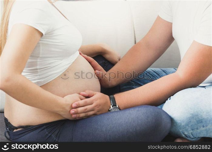 Closeup image of young couple expecting baby. Husband holding hands on big belly