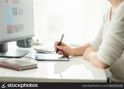 Closeup image of young female graphic designer holding stylus and working with graphic tablet. Closeup photo of young female graphic designer holding stylus and working with graphic tablet