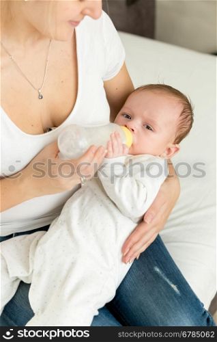 Closeup image of young mother feeding her baby boy in bed from bottle