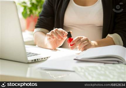 Closeup image of young woman painting fingernails at office