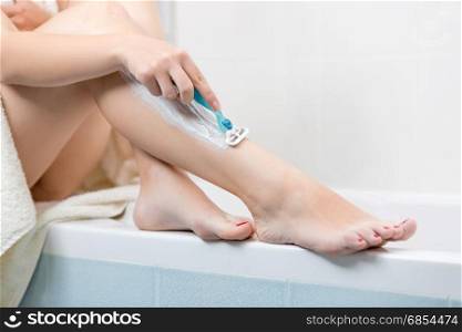 Closeup image of young woman shaving legs at bathroom
