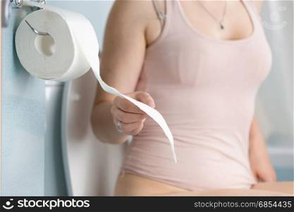 Closeup image of young woman tearing off toilet paper