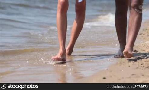 Closeup legs of couple walking in waters edge on beach leaving footprints in the sand on summer vacation