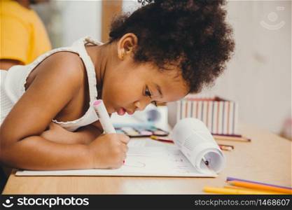 Closeup little child girl black skin writing doing homework at home.