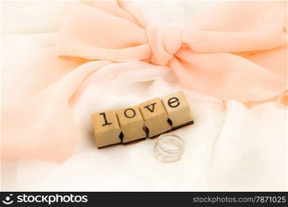 closeup love wording and rings on dress with peach bow ribbon, white soft textiles, wedding concept and idea