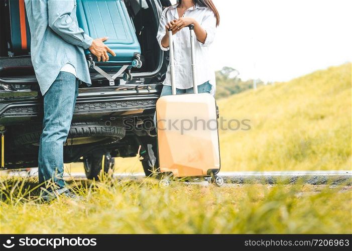 Closeup lower body of couple lift down trolly luggage at back of SUV car trunk along road trip with autumn mountain hill background. Freedom friend road way. Two people lifestyle transportation travel