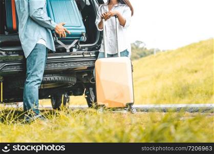 Closeup lower body of couple lift down trolly luggage at back of SUV car trunk along road trip with autumn mountain hill background. Freedom friend road way. Two people lifestyle transportation travel