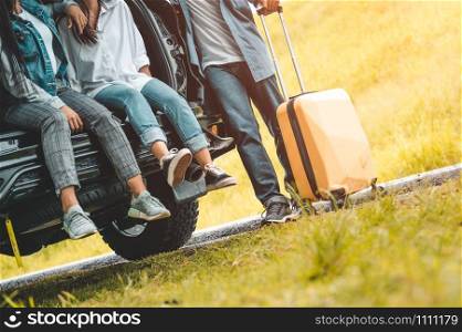 Closeup lower body of group of friends relaxing on SUV car trunk with trolly luggage along road trip with autumn mountain hill background. Freedom road way. People lifestyle transportation travel