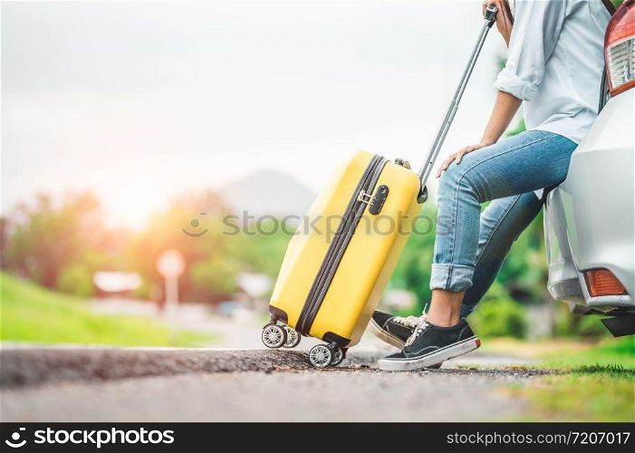 Closeup lower body of woman leg relaxing on car trunk with trolly luggage along road trip with autumn mountain hill background. Freedom road way. People lifestyle transportation travel in vacation