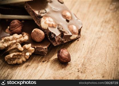 Closeup milk chocolate pieces and hazelnuts on wooden table.