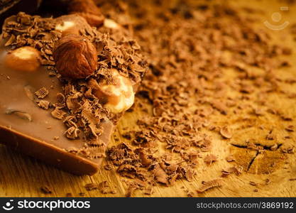 Closeup milk chocolate pieces hazelnuts and shavings curls on wooden table.