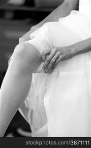 Closeup monochrome photo of young bride putting on white nylon stockings