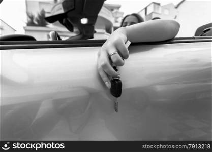 Closeup monochrome shot of young woman sitting in convertible and holding car keys